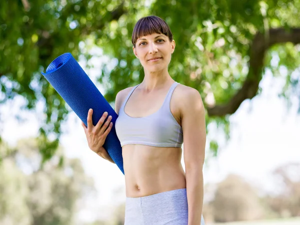 Jeune femme witth un tapis de gym dans le parc — Photo