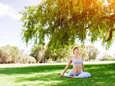 Genç kadın parkta yoga yapıyor.