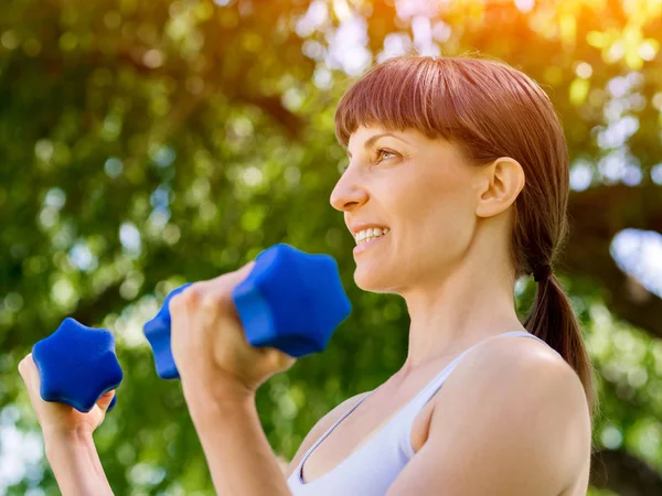 Porträt einer fröhlichen Frau in Fitnessbekleidung, die mit einer Hantel trainiert — Stockfoto