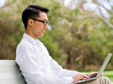 Genç işadamı açık havada otururken dizüstü bilgisayar kullanarak