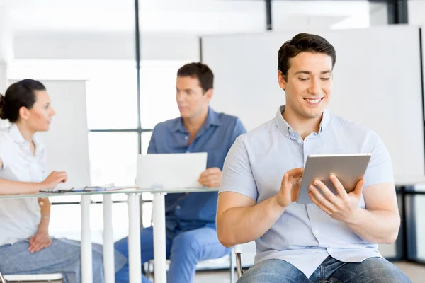 Joven hombre de negocios guapo usando su touchpad sentado en la oficina —  Fotos de Stock