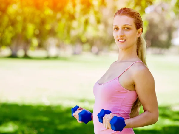 Porträt einer fröhlichen Frau in Fitnessbekleidung, die mit einer Hantel trainiert — Stockfoto