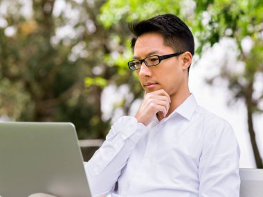 Genç işadamı açık havada otururken dizüstü bilgisayar kullanarak