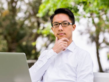 Genç işadamı açık havada otururken dizüstü bilgisayar kullanarak