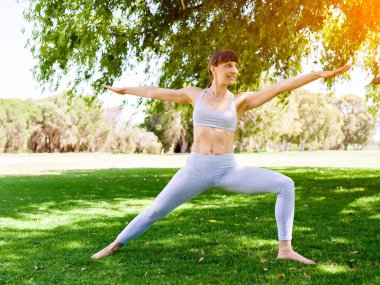 Genç kadın parkta yoga yapıyor.