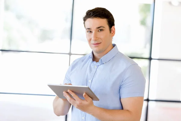 Joven hombre de negocios guapo usando su touchpad de pie en la oficina —  Fotos de Stock