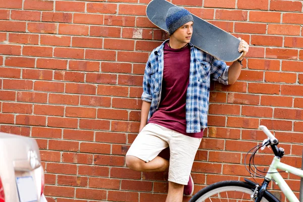 Мальчик-подросток со скейтбордом стоит рядом со стеной — стоковое фото