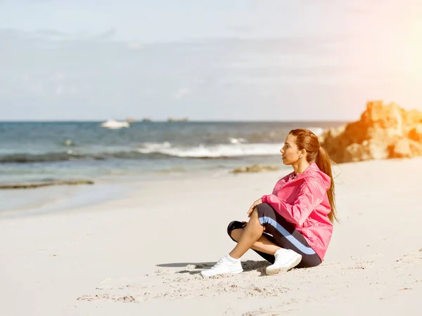 Mujer joven sentada en la playa en ropa deportiva — Foto de Stock