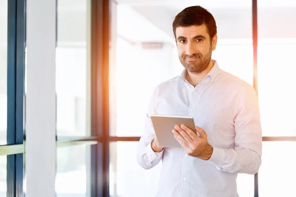 Jovem empresário bonito usando seu touchpad de pé no escritório — Fotografia de Stock