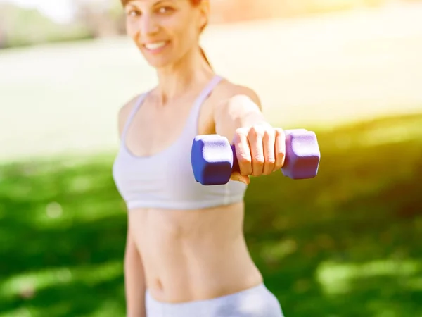 Porträt einer fröhlichen Frau in Fitnessbekleidung, die mit einer Hantel trainiert — Stockfoto