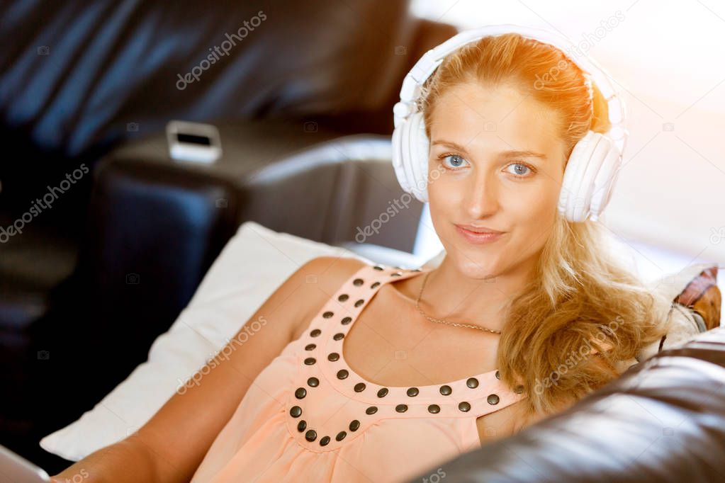 Young smiling woman with headphones relaxing on the sofa listening to music online using a smartphone