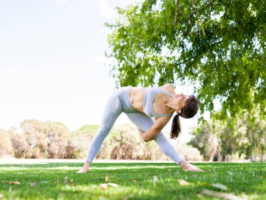 Genç kadın parkta yoga yapıyor.