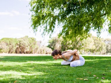 Genç kadın parkta yoga yapıyor.