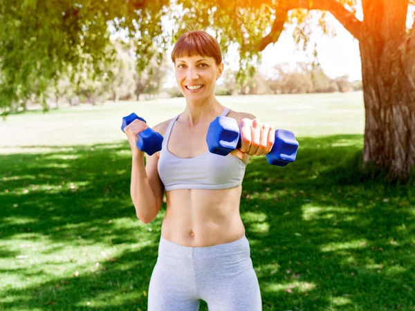 Retrato de mujer alegre en ropa de fitness haciendo ejercicio con mancuerna —  Fotos de Stock