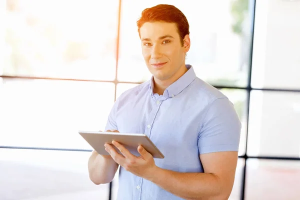 Młody przystojny biznesmen za pomocą jego stojące touchpad w biurze — Zdjęcie stockowe