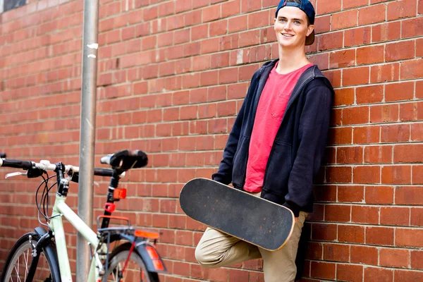Мальчик-подросток со скейтбордом стоит рядом со стеной — стоковое фото