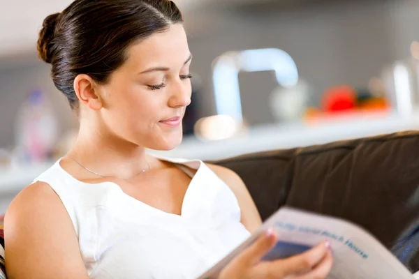 Ευτυχισμένη γυναίκα διαβάζει ένα περιοδικό που κάθεται σε έναν καναπέ — Φωτογραφία Αρχείου