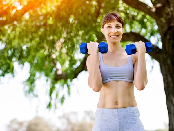 Porträt einer fröhlichen Frau in Fitnessbekleidung, die mit einer Hantel trainiert — Stockfoto