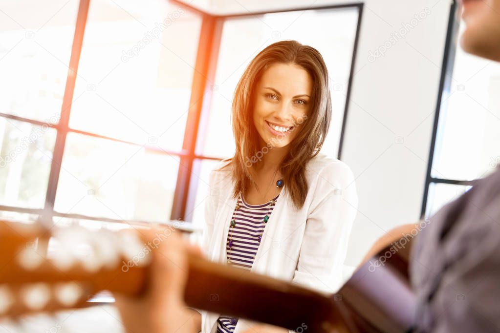 Young woman in office with friend playing guitar