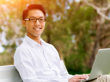 Genç işadamı açık havada otururken dizüstü bilgisayar kullanarak