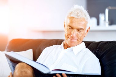 Yakışıklı sennior adam bir kanepe üzerinde rahatlatıcı bir kitap okuma