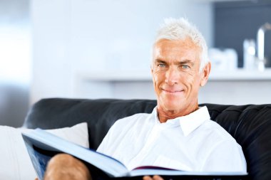 Yakışıklı sennior adam bir kanepe üzerinde rahatlatıcı bir kitap okuma