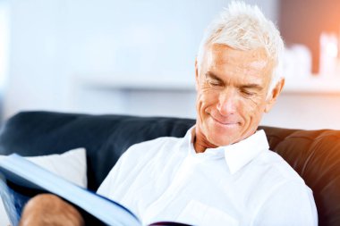 Yakışıklı sennior adam bir kanepe üzerinde rahatlatıcı bir kitap okuma