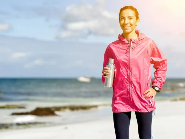 Mooi meisje in de sport kleding drinkwater na training op het strand — Stockfoto