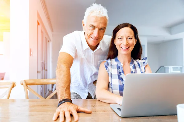 Heureux couple d'âge mûr moderne travaillant sur ordinateur portable à la maison — Photo