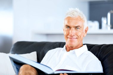 Yakışıklı sennior adam bir kanepe üzerinde rahatlatıcı bir kitap okuma