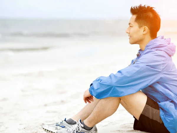 Молодой человек сидит на пляже в спортивной одежде — стоковое фото