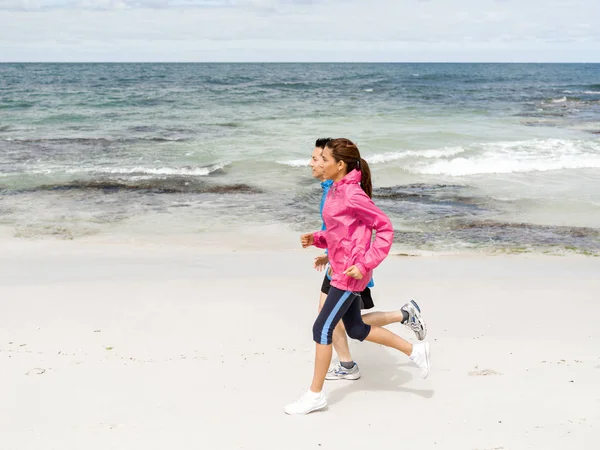 Pareja joven corriendo a lo largo de la orilla del mar —  Fotos de Stock