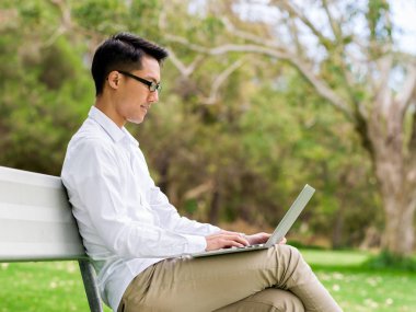 Genç işadamı açık havada otururken dizüstü bilgisayar kullanarak