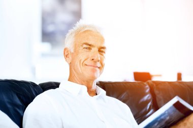 Yakışıklı sennior adam bir kanepe üzerinde rahatlatıcı bir kitap okuma