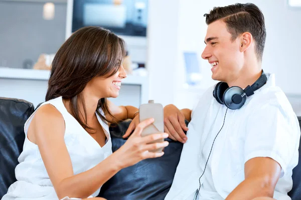 Młoda para patrząc na telefon komórkowy siedząc w domu — Zdjęcie stockowe