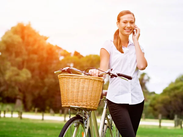 Hermosa joven rubia con bicicleta en el parque hablando por teléfono — Foto de Stock