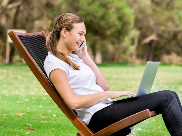 Mujer de negocios joven sentado en el parque y trabajando con el ordenador portátil —  Fotos de Stock