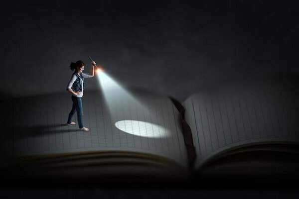 Woman with flashlight standing on pages of huge book. Mixed media