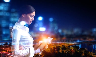 Büyüleyici genç iş kadını tablet kullanıyor, yazıyor, bir şeyler arıyor. Zarif bluz giymiş, gözlüklü.