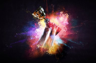 Elinde altın bir kupa var, arka planda.