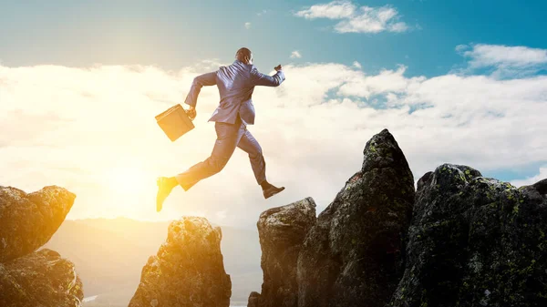 Vista trasera del hombre de negocios negro saltando sobre piedras de montaña — Foto de Stock