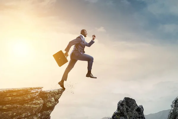 Homem de negócios preto pulando sobre pedras de montanha — Fotografia de Stock