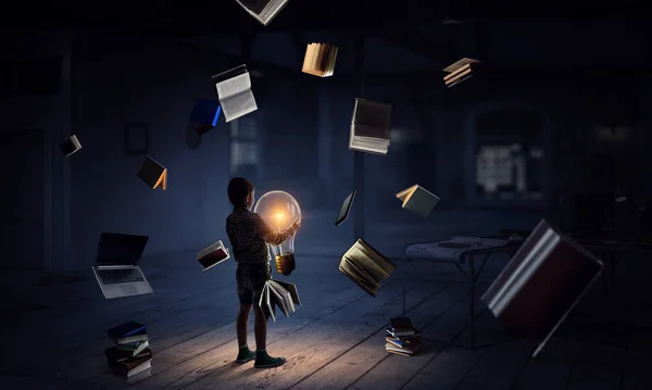 Boy holding a light bulb with books around him — Stock Photo, Image