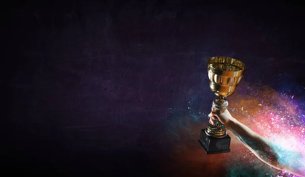 Hand holding up a gold trophy cup against dark background — Stock Photo, Image