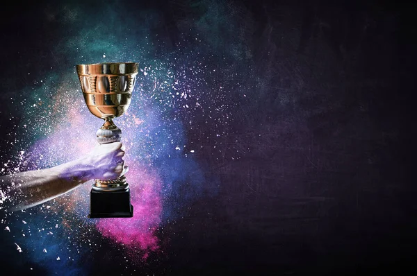 Hand holding up a gold trophy cup against dark background — Stock Photo, Image