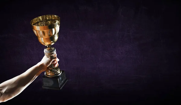 Kézfogás egy arany trófea csésze ellen sötét háttér — Stock Fotó