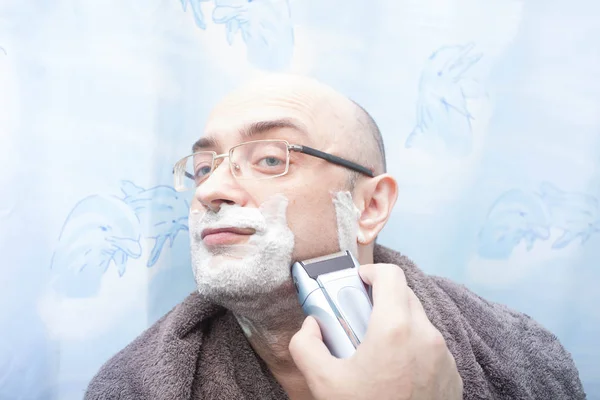 Smiling man shaving his beard with electric razor