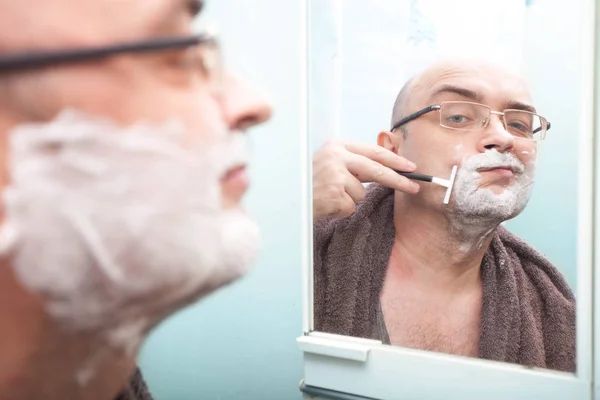 Sorrindo cara de óculos barbeando sua barba com lâmina descartável — Fotografia de Stock