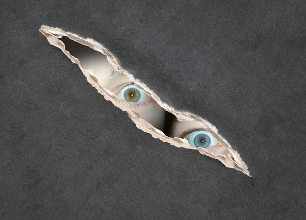 Olhos de duas crianças olhando através de um buraco no papel — Fotografia de Stock
