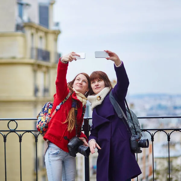 两个性格开朗的女孩，在巴黎以自拍照在蒙马特尔上使用移动电话 — 图库照片